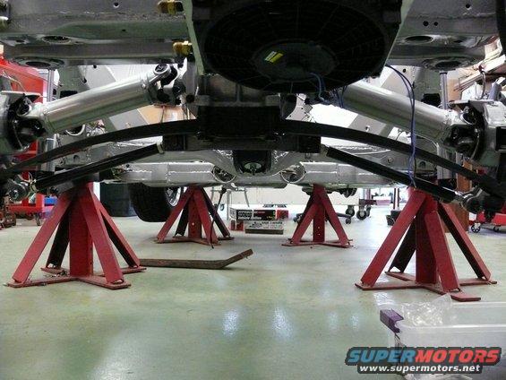 Car underbody with drivetrain components visible, supported by red jack stands