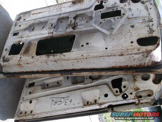 Two white car doors, rusted and weathered, stacked on top of each other. Handwritten text is visible on both