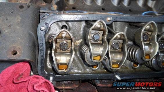 Close-up of engine valve train with rocker arms and springs visible. A red rag is in the lower left