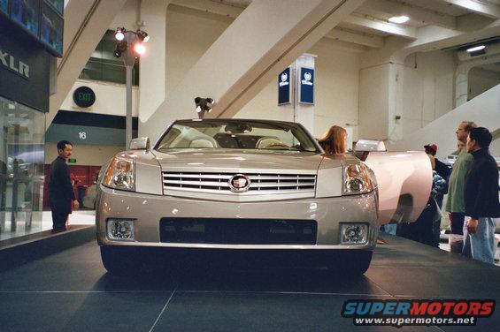 Silver Cadillac XLR convertible with chrome grille and headlights, viewed from the front at an auto show