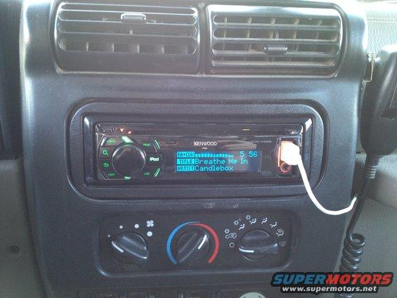 Kenwood stereo in car dashboard with air vents above. iPod cable plugged in