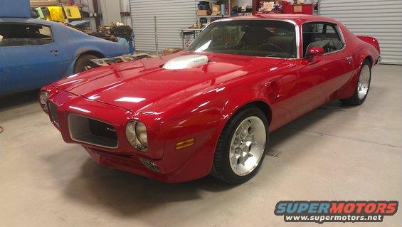 Red Pontiac Firebird with a silver hood scoop, custom wheels, and a blue car in the background
