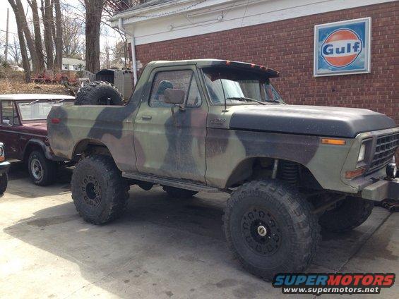 Camouflaged 1979 Ford Bronco with lifted suspension and large tires parked next to another vehicle