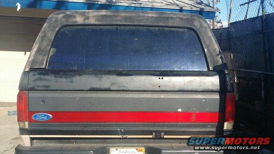 Rear of a Ford Bronco with a red stripe and a camper shell. The Ford logo is visible