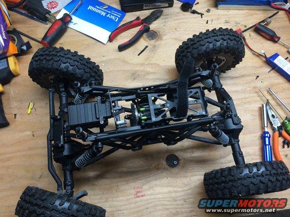 remote control rock crawler chassis with suspension and drivetrain components visible, tools and manual on workbench