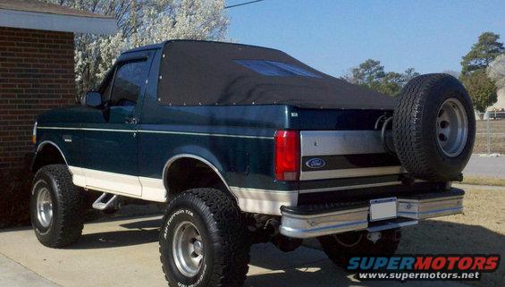 Dark green Ford Bronco with a black soft top and spare tire on the back