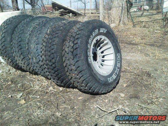 Four off-road tires with Nexen Roadian MT tread, mounted on silver alloy wheels, resting on the ground