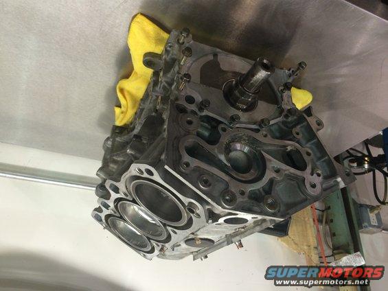 Engine block with yellow cloth on a metal surface. Supermotors.net logo visible