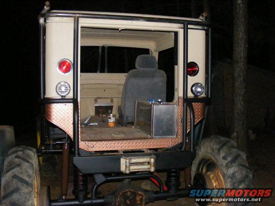 Off-road vehicle rear view, tan body, diamond plate accents, roll cage, large tires, winch