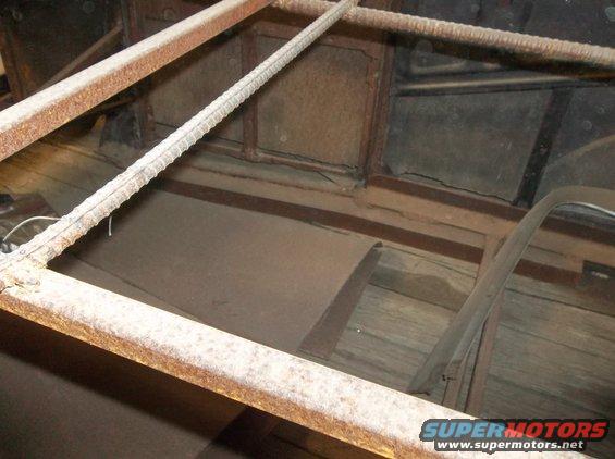 Interior view of a rusty car frame with wooden floorboards and a partial window frame