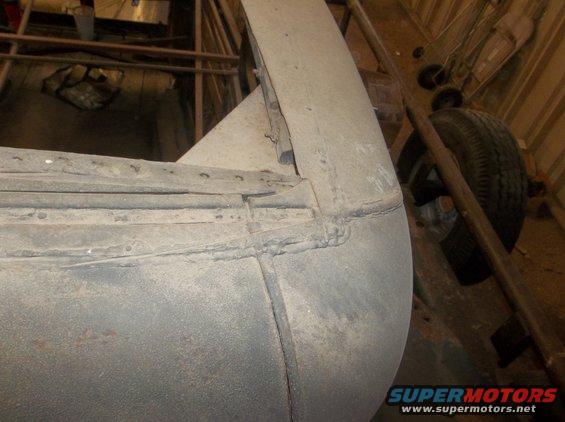 Close-up of a car's rear fender and wheel well, showing metalwork and a tire