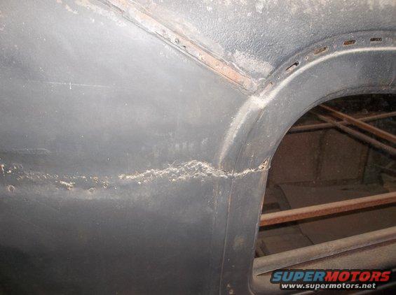 Close-up of a dark gray car body panel showing a seam with rust and dirt buildup