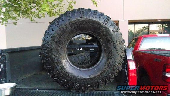 Spare tire in the bed of a black pickup truck next to a red pickup truck