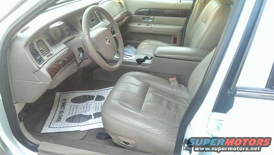 Interior of a 2000 Mercury Grand Marquis showing tan leather seats, dashboard, and steering wheel. Floor mat says 'Thanks for coming in.'
