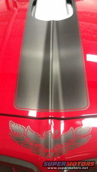 Red car hood with a black carbon fiber stripe and a silver bird decal. The car appears to be a 1970s Pontiac Firebird or Trans Am
