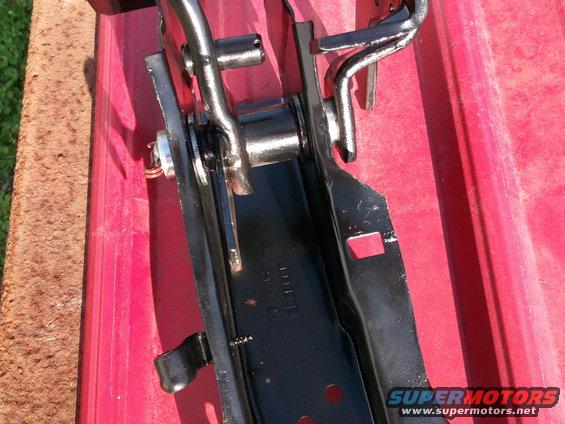 Black metal car part with chrome hinges against a red surface