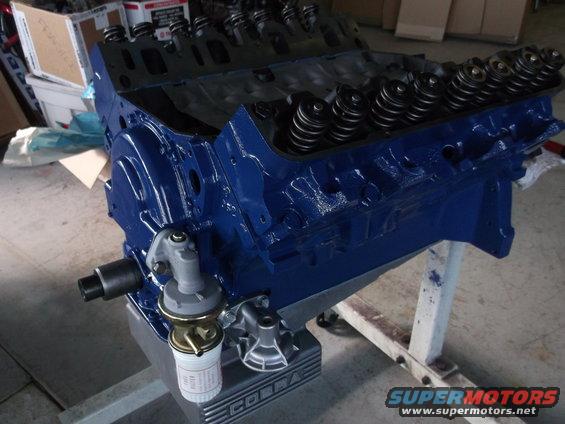 Blue engine block with valve springs and a fuel pump, resting on an engine stand