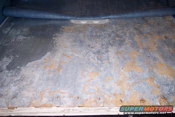 Corroded metal floor panel with some blue carpet material rolled up at the top