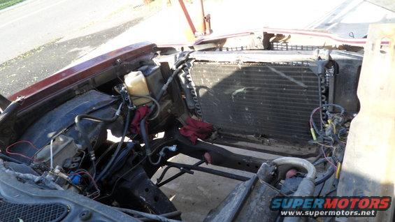 Car engine bay with radiator and some engine components removed, showing the frame and hoses