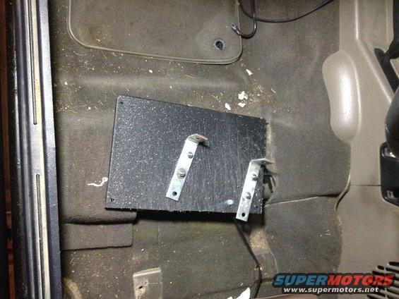 Black textured bracket with metal L-brackets mounted on a dirty vehicle carpet floor