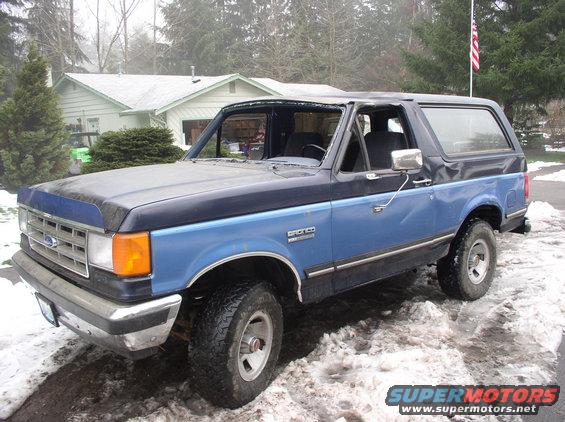 Blue and black Ford Bronco parked in snow. Has a removable top