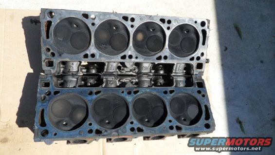 Two engine cylinder heads with visible valves and combustion chambers, resting on a surface