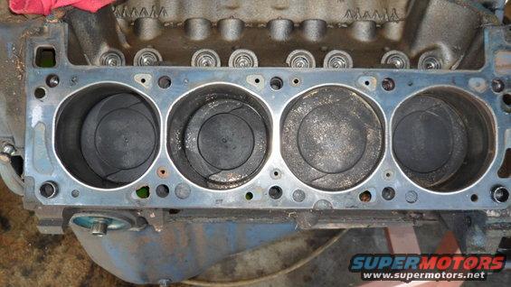 Engine block showing four pistons inside cylinders. Some carbon buildup visible