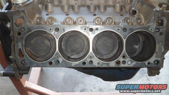 Engine block with four visible pistons, some showing carbon buildup and cracks