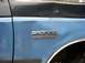 1988 Ford Bronco - Close-up of a blue Ford Bronco XLT emblem on the side of a vehicle with a black roof and visible damage.