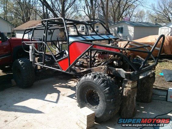 Custom buggy frame with red panels and large off-road tires, on blocks
