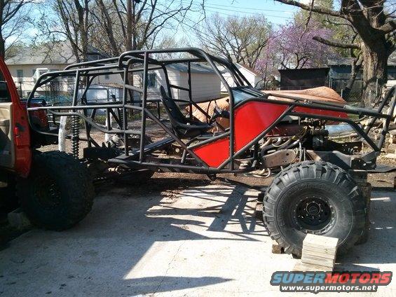 Custom off-road buggy frame with large tires, engine visible, red body panels, and roll cage. It is on blocks