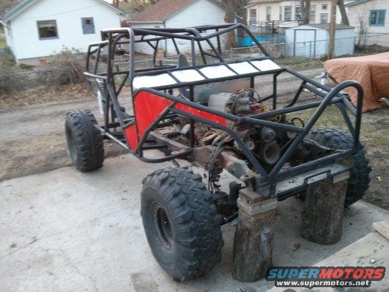 Custom buggy frame with large tires, engine visible, and red side panels. Vehicle is on blocks