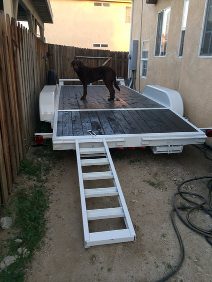 Trailer with wooden deck and a brown dog standing on it. Ramp is extended