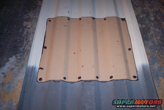 Corrugated metal panel with a rectangular cutout, secured by screws. It's placed on a larger corrugated surface