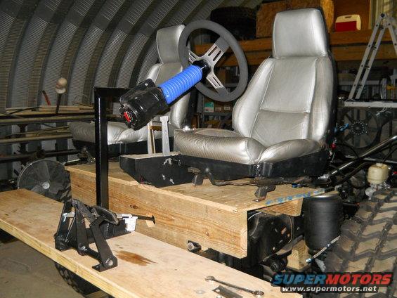 Custom interior with two silver bucket seats, steering wheel, and shifter on a wooden platform