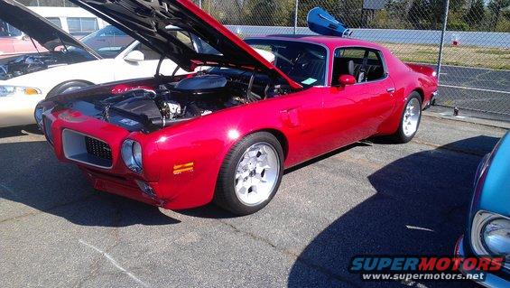 red muscle car, hood open, showing engine. Another car is parked next to it