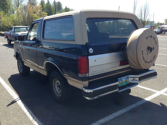 Rear view of a dark blue and tan Ford Bronco with a spare tire cover. License plate reads 929 AKY. Another truck is parked behind it