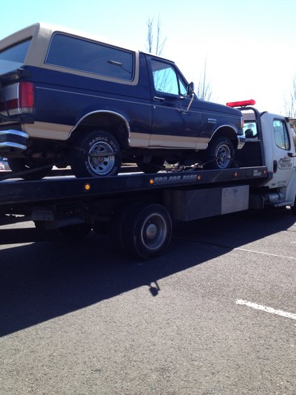 Dark blue and tan Ford Bronco on a flatbed tow truck, side view