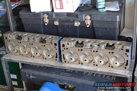 Two engine cylinder heads sitting on a shelf, behind a toolbox