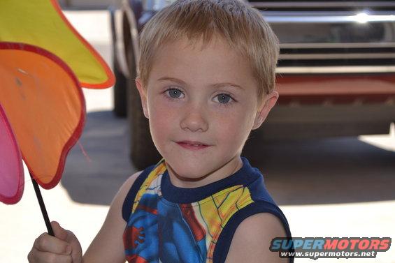 Young boy holding a colorful pinwheel. A vehicle is partially visible in the background