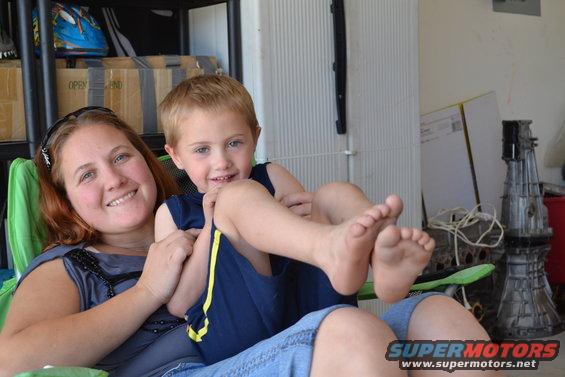 Woman and child sitting in a garage with boxes and car parts in the background