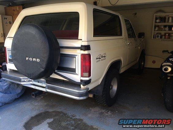 White Ford Bronco parked in garage, spare tire on back, 4x4 badge on fender
