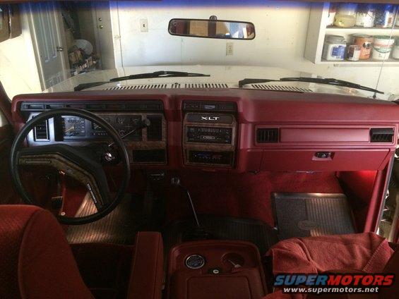Red interior of a 1980s Ford Bronco showing dashboard, steering wheel, and center console