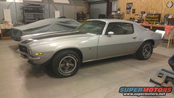 Silver 1976 Pontiac Trans Am with black stripes in a garage, another car covered in the background