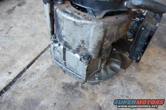 Grubby engine component with black plastic connector attached, on concrete floor