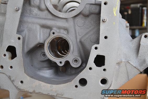 Gray metal engine block with circular openings and bolt holes. A silver ring is visible inside one opening