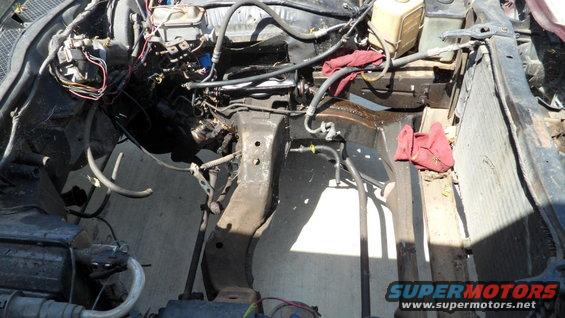 Engine bay of a car, showing the frame, hoses, and wiring. Some red rags are visible
