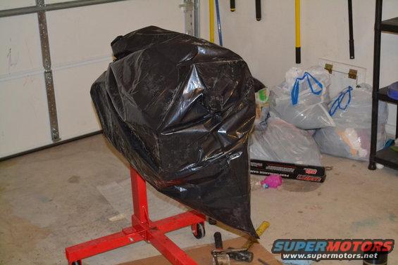 Engine on a red engine stand covered by a black tarp in a garage. Bags of items are in the background