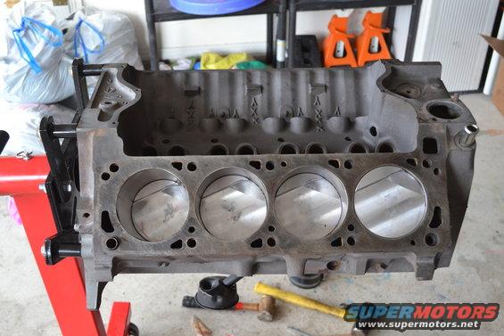 Engine block on a stand, showing cylinder bores. Tools and garage items in background