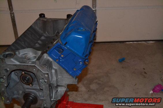 Engine block with a bright blue valve cover on a stand. Some bolts are visible on the valve cover